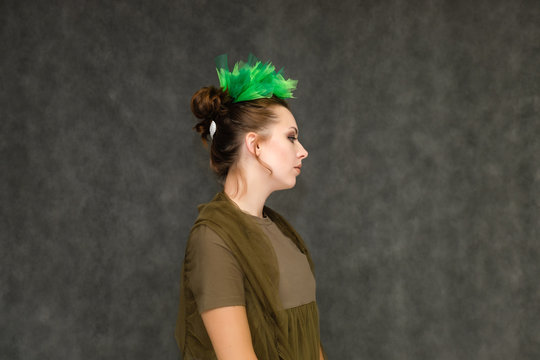 Portrait in lower chest on a gray background of a pretty young brunette woman with a green floral wreath in her hair. Standing in different poses, talking, showing hands, demonstrating emotions.