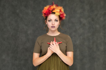 Portrait in lower chest on a gray background of a pretty young brunette woman with a red floral wreath in her hair. He stands with a starfish in his hands, talking, with emotions.