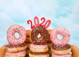 Variety of glazed donuts stacked with 2020 year candles, blue background sky with clouds. Happy New Year theme.