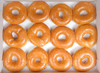 Top view flat lay of plain glazed donuts in a white box isolated. One dozen donuts. The original...