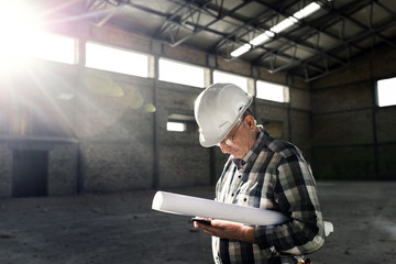 Senior construction worker with blueprint controlling building site.