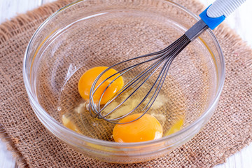 Eggs in a bowl with whisk on a wooden table