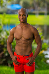 Handsome shirtless male fitness model posing in the park. Blurry background