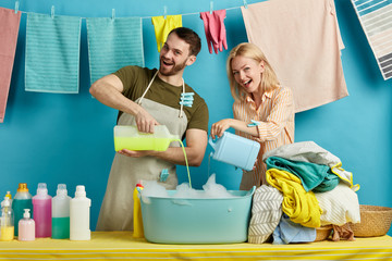 pleasant young couple preparing water fow washing clothes by hand, isolated blue background. table...