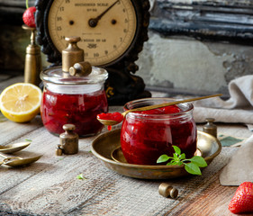 Two glass jars with homemade canned strawberry jam, marmalade, jelly on rustic wooden grey table with basil