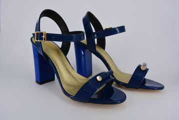 Colored elegant women's sandals from natural patent leather and zotoli insoles. Fashionable dark blue sandals with high, wide heels with a broom and gold clasps.