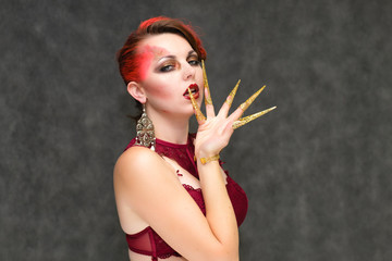 Obraz premium Portrait to the waist on a gray background of a pretty young brunette woman with beautiful makeup, with gold jewelry on her hand. Art, beauty, great makeup. Shows emotions.