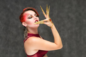 Obraz premium Portrait to the waist on a gray background of a pretty young brunette woman with beautiful makeup, with gold jewelry on her hand. Art, beauty, great makeup. Shows emotions.