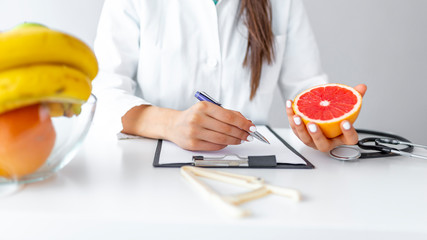 Nutritionist writing diet plan for patient, panorama, copy space. Female nutritionist with fruits...