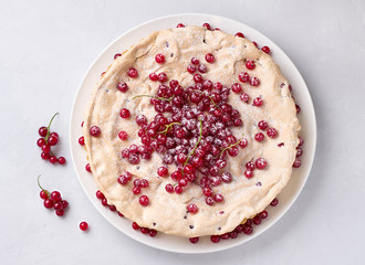 Delicious homemade tart with red currants and meringue, decorated with fresh berries, sprinkled with powdered sugar on a white plate on a light gray background, top view
