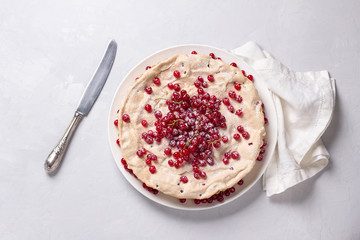 Delicious homemade tart with red currants and meringue, decorated with fresh berries, sprinkled with powdered sugar on a white plate on a light gray background, top view
