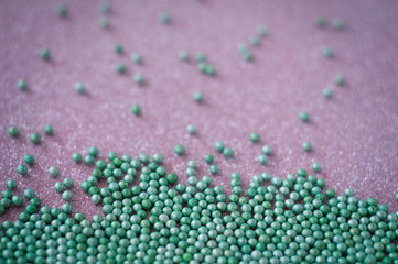 Green ball crystal sugar sprinkle dots, on glitter pink background, decoration for confectionery.  Sugar, sweetness, diabetes concept.
