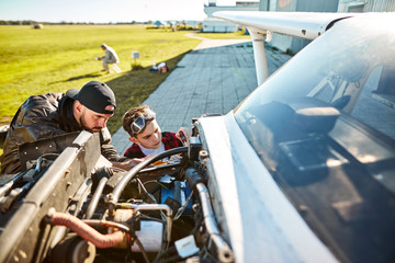 little boy in aviator glasses and with screwdriver helps his father pilot to fix broken engine of...