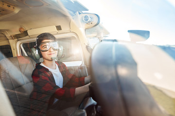 photo made through the window of light private airplane, where happy cute boy sits in pilot headset, waiting with excitement and joy for his first flight. © alfa27