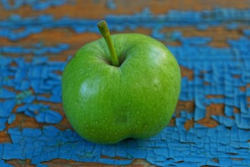 one big green apple lying on a blue scuffed board