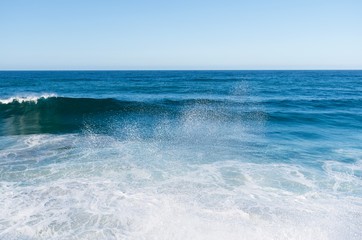Blue ocean waves crash on a tetrapods breakwater forming white foam.