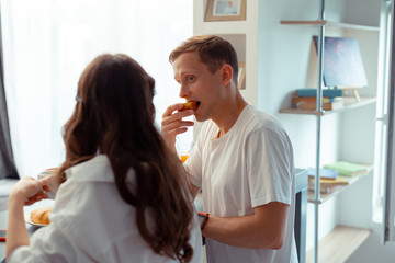 Blue-eyed husband biting apple while having breakfast with wife