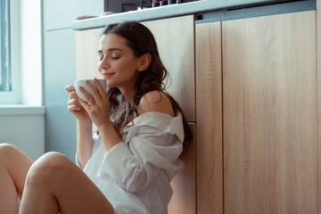 Curly woman smelling coffee while having breakfast