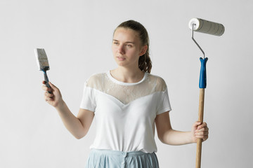 Young happy woman painting interior wall with paint roller in new house. A woman with roller applying white paint on a wall. 