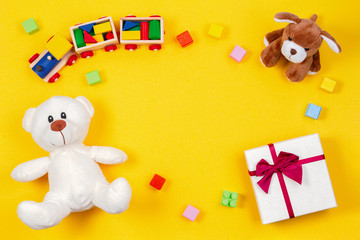 Kids baby toy background. Teddy bear, toy train, present gift box and other toys on yellow background