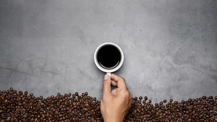 hand holding cup of coffee with beans on concrete background