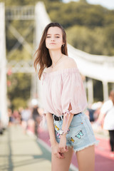 Brunette young woman in pink blouse, jean skirt gladly posing while walk outside in good mood.  Close up portrait of romantic stylish woman.