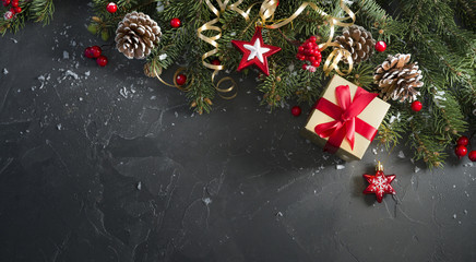 Christmas dark black background with beautiful texture and Golden gift box with red ribbon, serpentine, fir branches, cones, Christmas tree toys stars, top view, copy space.
