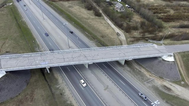 Slow top view of wide grey roads with billboards, fast moving cars and trucks, deserted dust fields, bridges with cracked asphalt, in less populated urban area of large city on cloudy cold day.