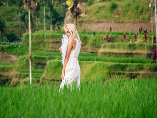 Fototapeta na wymiar Blondie girl in straw hat and white dress on the rice fields