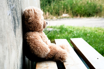 Teddy bear toy on the bench at the concrete wall with small tic tac toe game