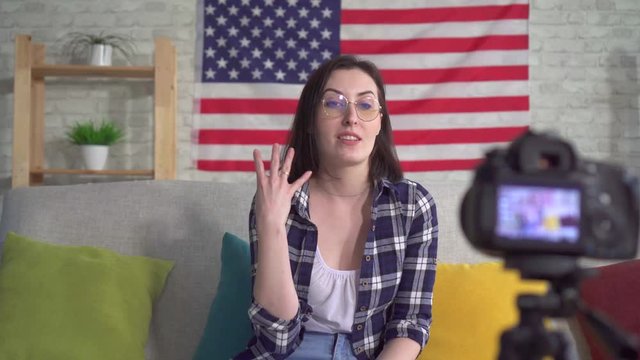 Young woman blogger in shirt on American flag background recording video