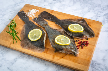 Fresh uncooked flounder fish with spices on wooden board