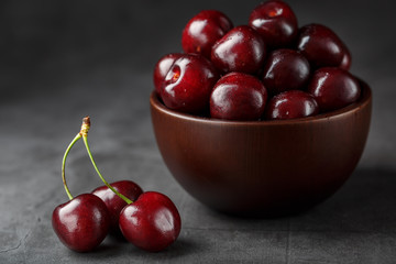 Ripe and juicy cherry berries on a black textural background in a brown cup, with water drops. Top view, close-up.