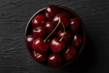 Ripe and juicy cherry berries on a black textural background in a brown cup, with water drops. Top view, close-up.