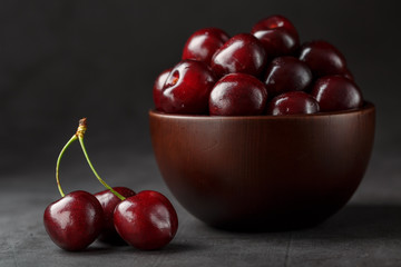 Ripe and juicy cherry berries on a black textural background in a brown cup, with water drops. Top view, close-up.