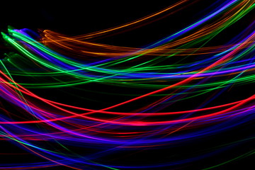 Long exposure photograph of neon multi colour in an abstract swirl parallel lines pattern against a black background. Light painting photography.