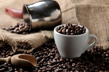 Roasted coffee beans in a cup and wooden spoon on a black background. Robusta, Arabica.