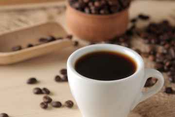 Coffee in a white cup and roasted coffee grains on a natural wooden table. Robusta, Arabica. close-up