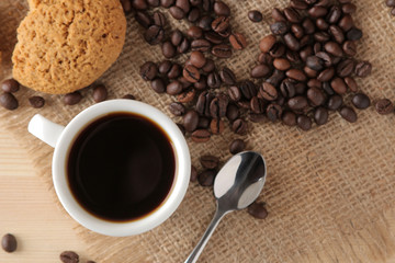 Coffee in a white cup and roasted coffee beans and biscuits on a natural wooden table. Robusta, Arabica. top view