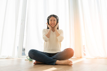 relex and peaceful asian woman enjoy weekend with music headphone morning sunlight near window home background