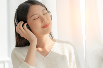 relex and peaceful asian woman enjoy weekend with music headphone morning sunlight near window home...