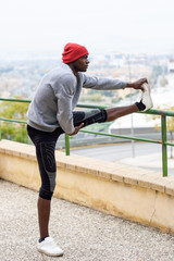 Black man doing stretching before running in urban background