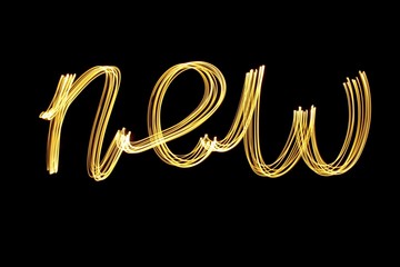 Long exposure photograph of metallic gold colour spelling the word 'new' against a black background. Light painting photography, happy new year series.
