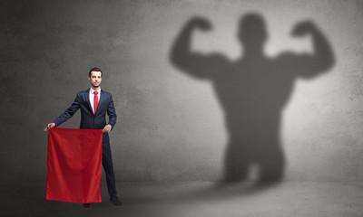 Businessman standing with red cloth on his hand and strong hero shadow on the background