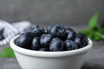 Bowl of tasty blueberries on grey table, closeup