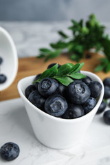 Bowl of tasty fresh blueberries and leaves on stone board, space for text