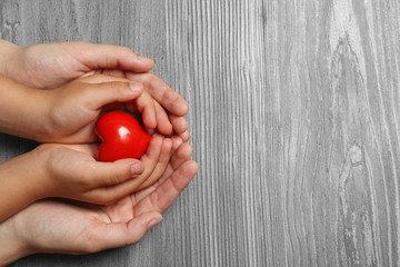 Woman and child holding heart on wooden background, top view with space for text. Donation concept