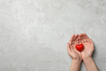 Woman holding heart on grey stone background, top view with space for text. Donation concept