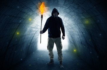 Ugly man with burning flambeau walking in a dark tunnel