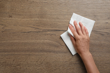Woman wiping wooden table with paper towel, top view. Space for text